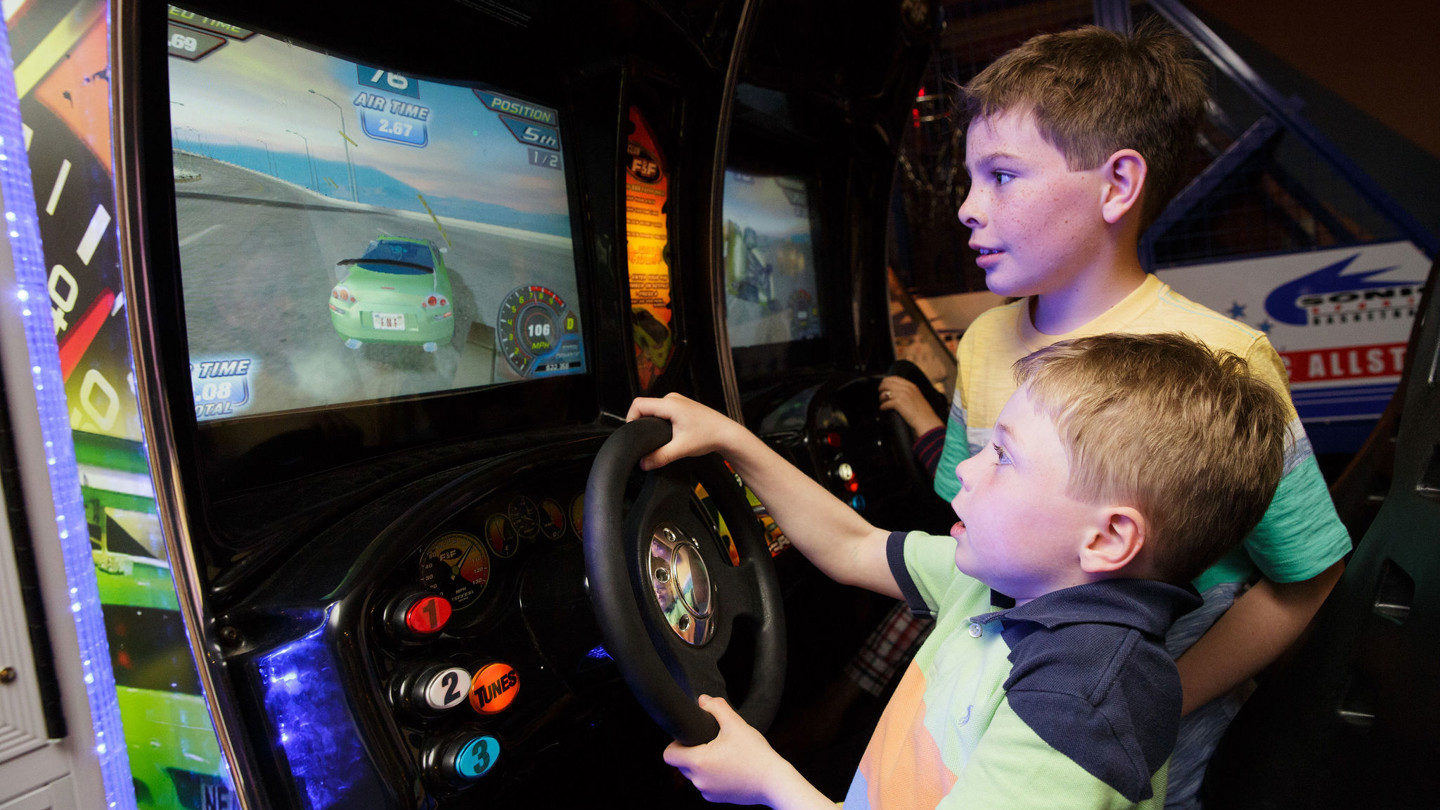 Two boys play a driving arcade game