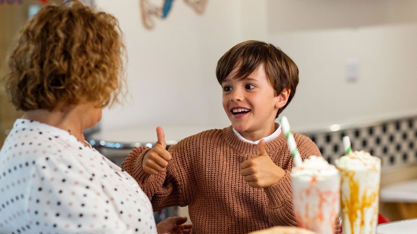 Young boy puts his thumbs up whilst enjoying a milkshake