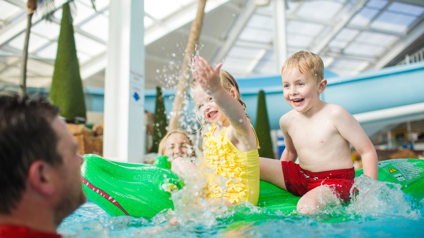 You girl splash water at family whilst on a crocodile inflatable