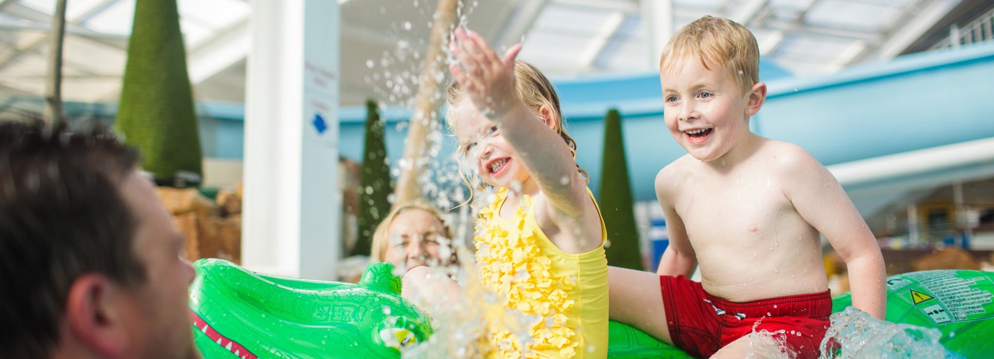 You girl splash water at family whilst on a crocodile inflatable